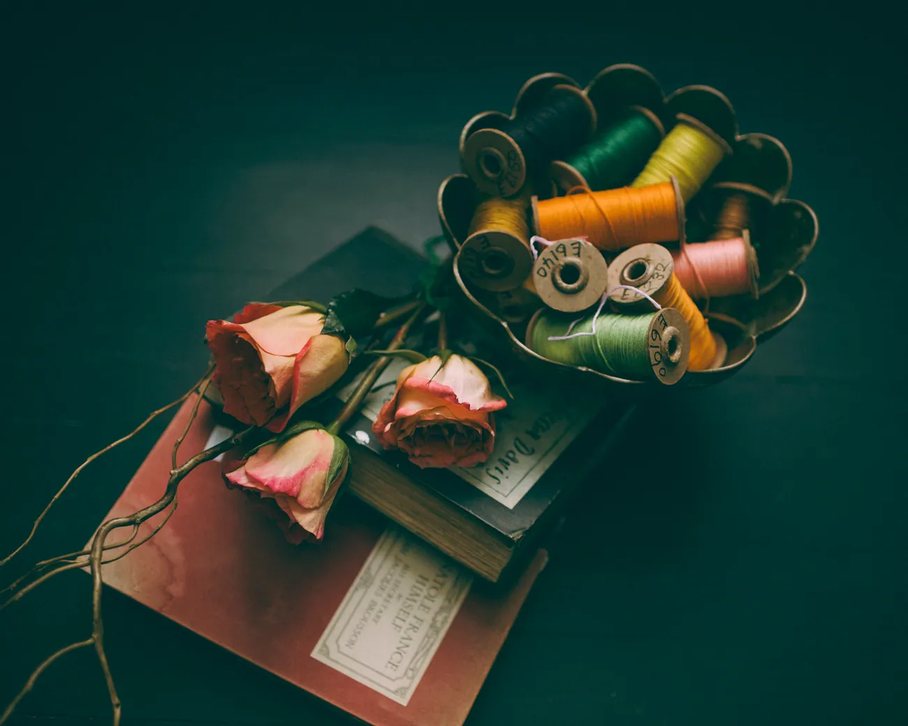 Pink roses on old books beside spools of thread